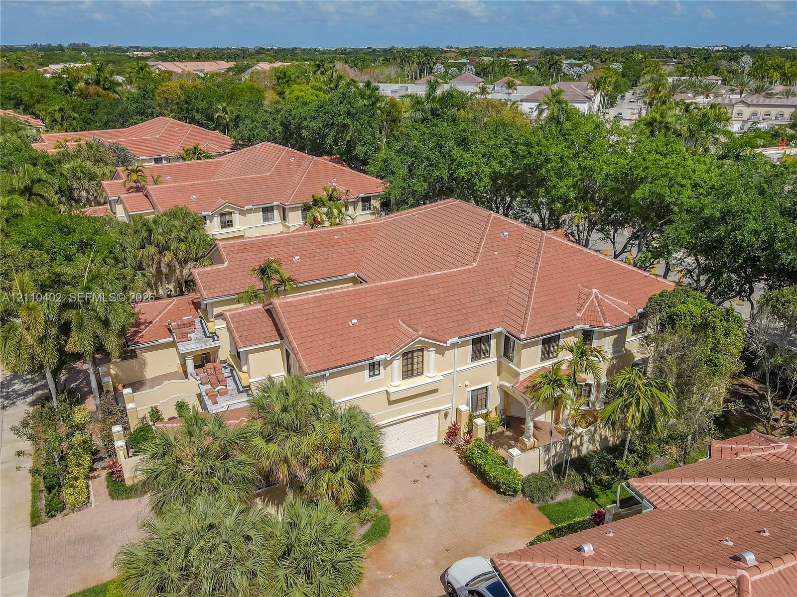 Multi-level residence featuring a clay tile roof, stucco exterior, attached multi-car garage, paved driveway, and established landscape