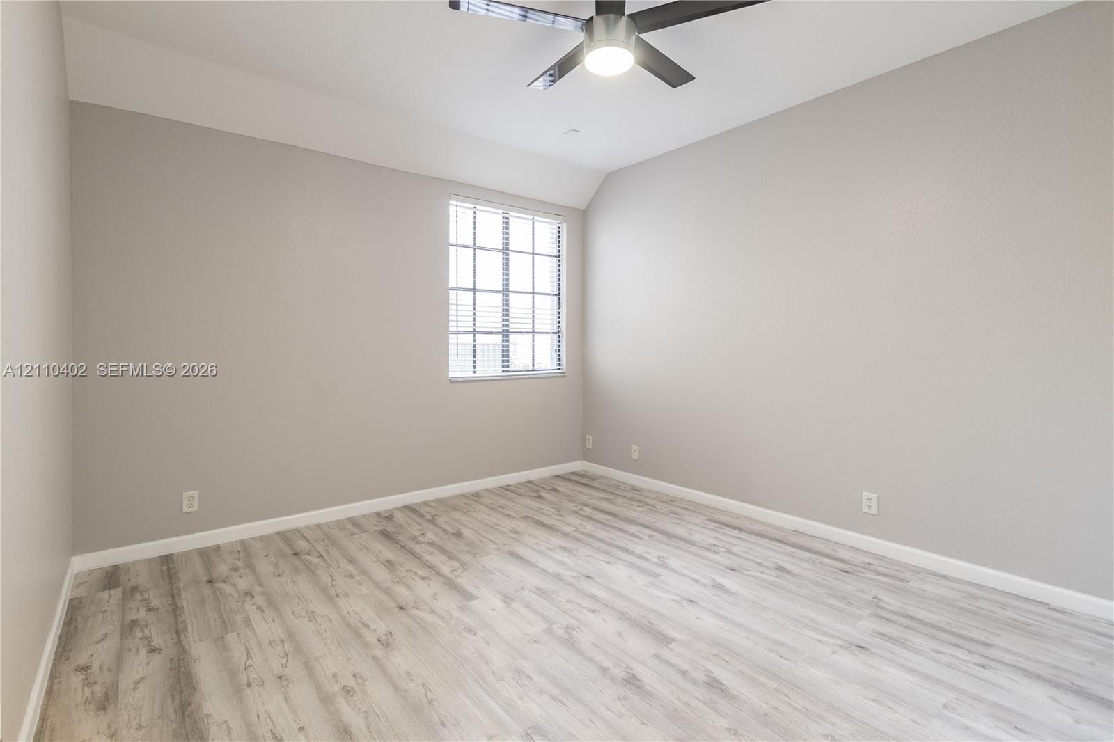 Room with wood-finish flooring, neutral wall paint, multi-pane window, and a ceiling fan with integrated lighting
