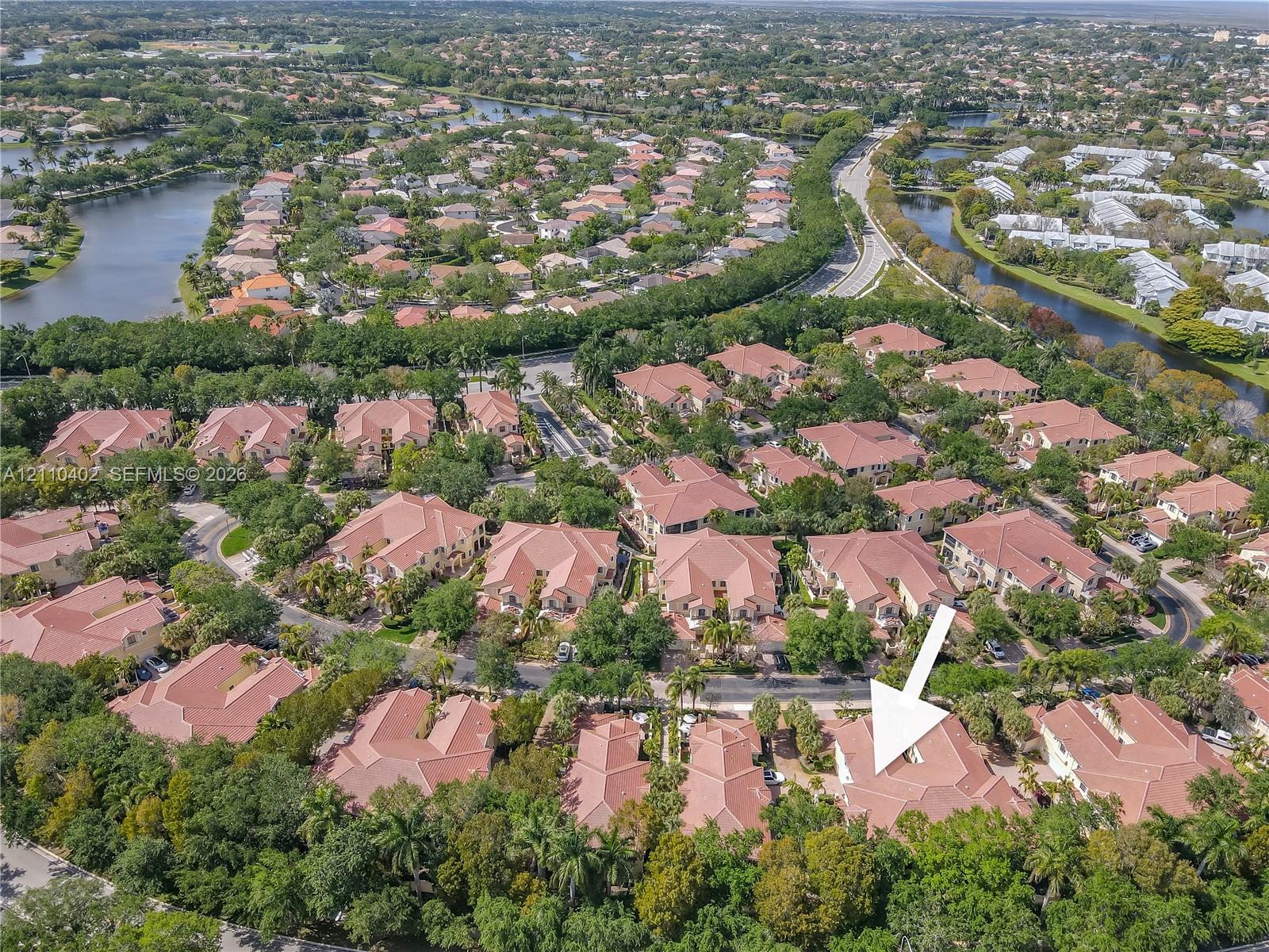 Aerial perspective of a multi-unit residential property featuring tile roofing, mature landscaping, and surrounding canal waterways
