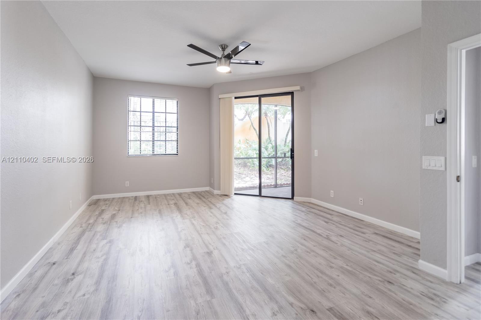 Neutral-toned interior featuring wood-finish flooring, a multi-pane window, a ceiling-mounted light fixture with fan, and a sliding glass door
