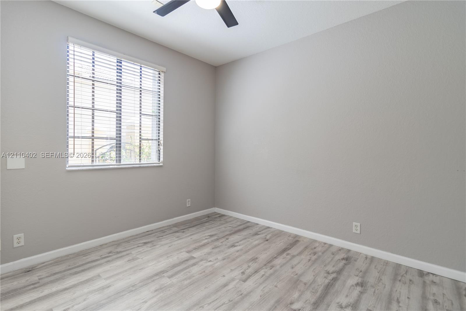 Room featuring wood-finish flooring, neutral wall paint, a multi-pane window with horizontal blinds, and a matte black ceiling fan