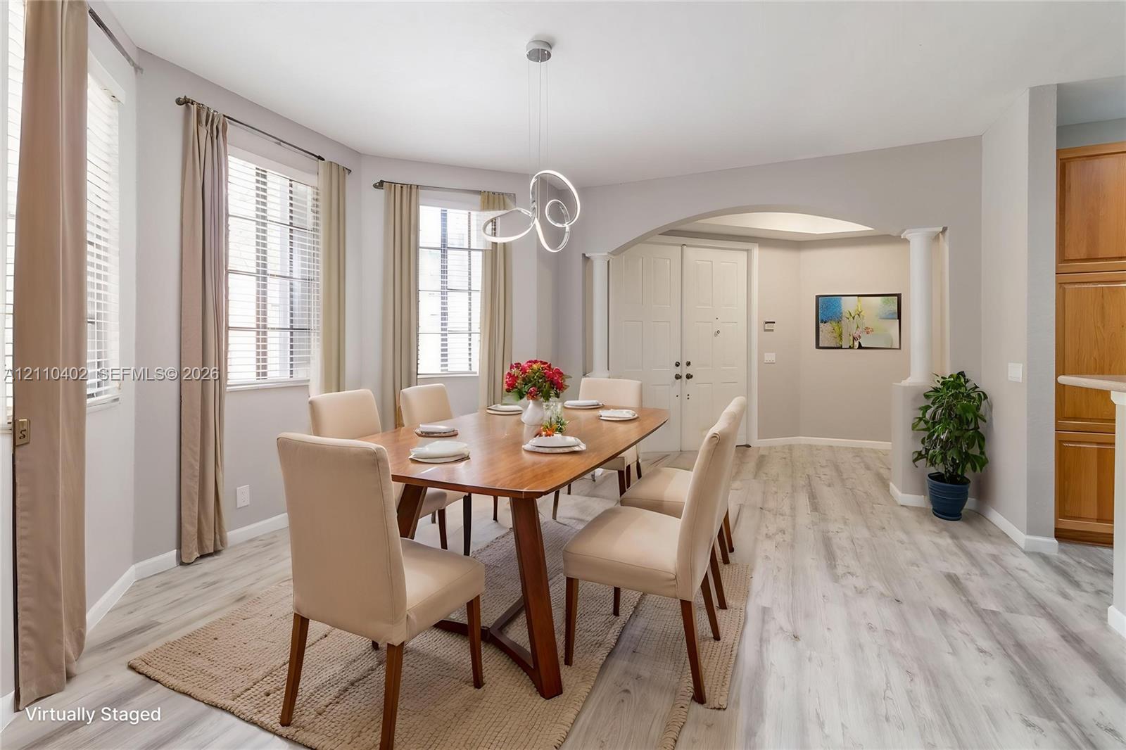 Wood-finish flooring, architectural arched opening with decorative columns, modern multi-ring pendant lighting, and abundant natural light from multiple large windows