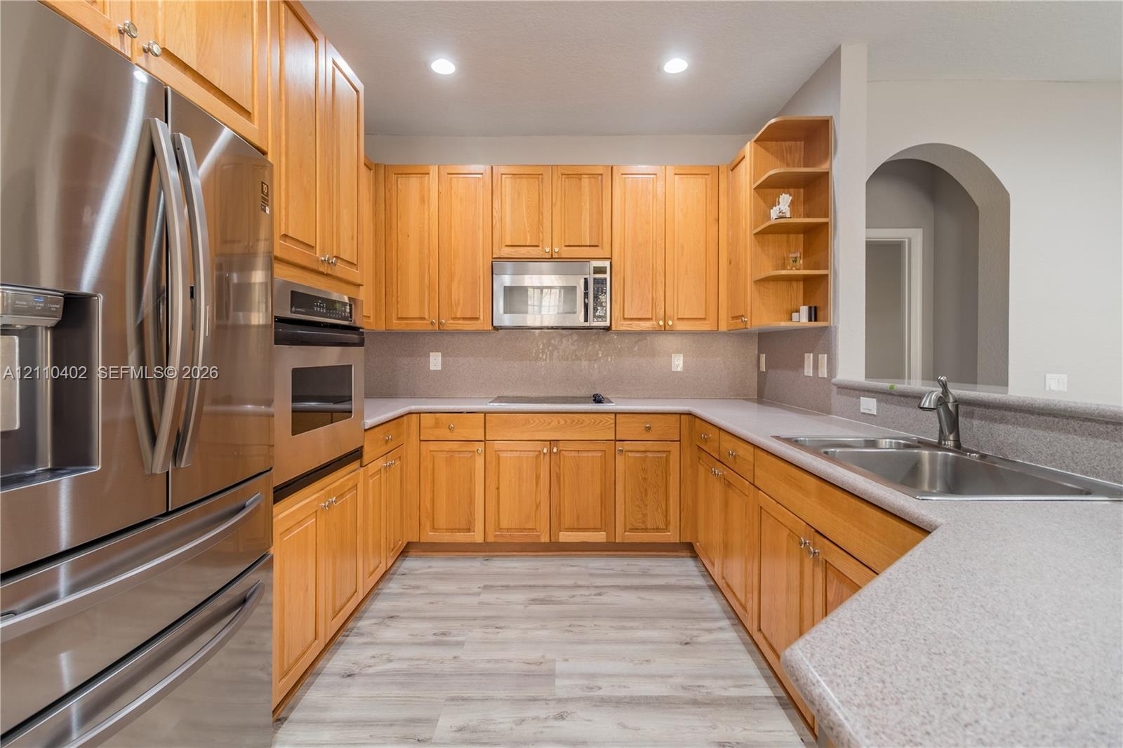 Kitchen featuring light wood cabinetry, stainless steel appliances, solid surface countertops, recessed lighting, and wood-finish flooring