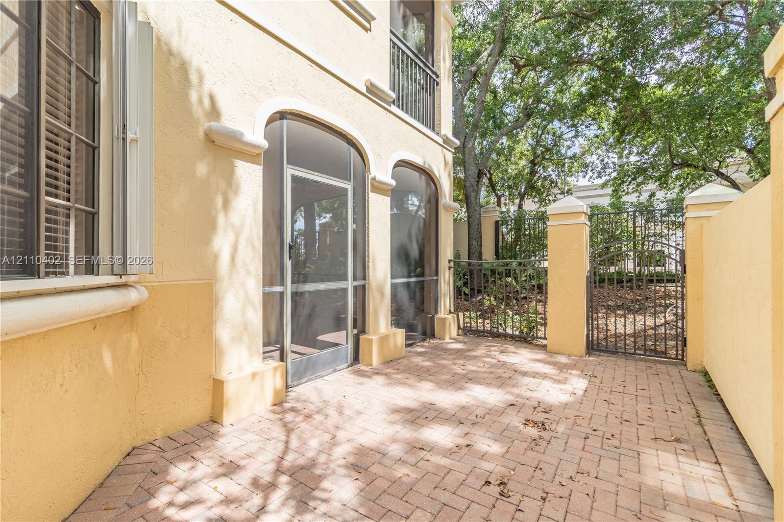 Stucco exterior featuring arched screened entryways, a herringbone-patterned brick patio, and a decorative metal gate enclosure