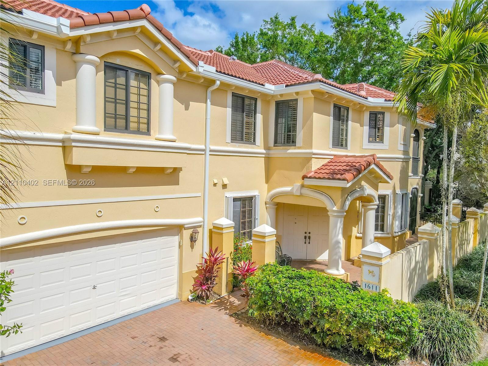 Mediterranean-inspired exterior featuring a clay tile roof, stucco facade, decorative columns, brick-paved driveway, and integrated two-car garage