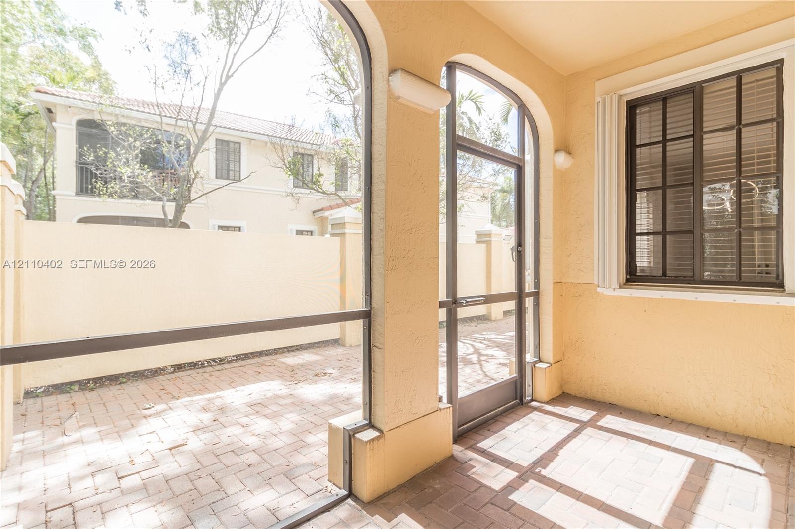 Screened patio featuring a paver floor, arched structural openings, and a grid-pattern window with a light-colored stucco exterior