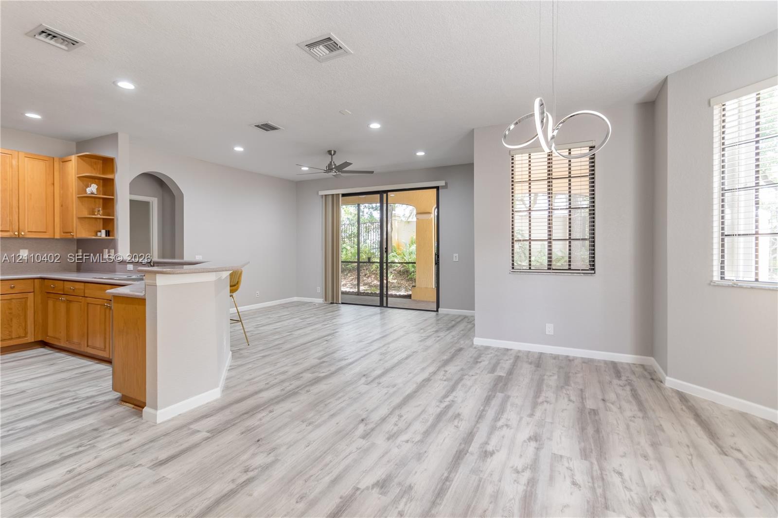 Open-concept interior featuring wood-finish flooring, wood cabinetry, recessed lighting, a modern geometric pendant light, and sliding glass doors
