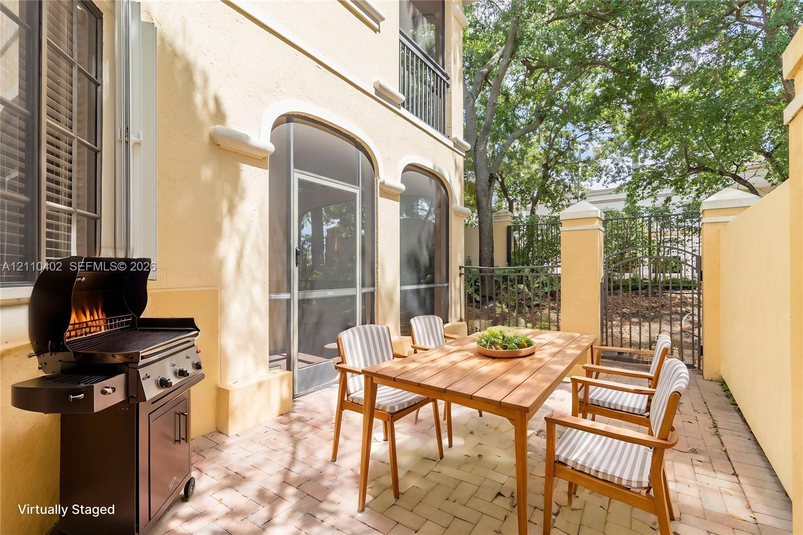 Private courtyard patio featuring brick pavers, arched architectural detailing, a screened enclosure, and wrought-iron fencing