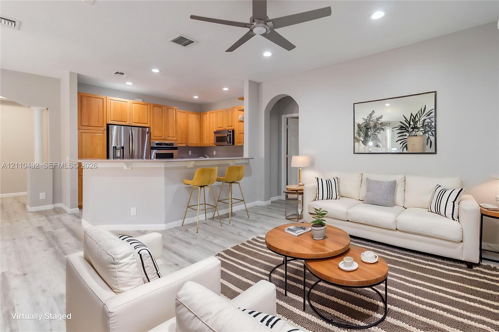 Open-concept floor plan featuring wood-finish flooring, recessed lighting, a breakfast bar, stainless steel appliances, and an arched architectural opening