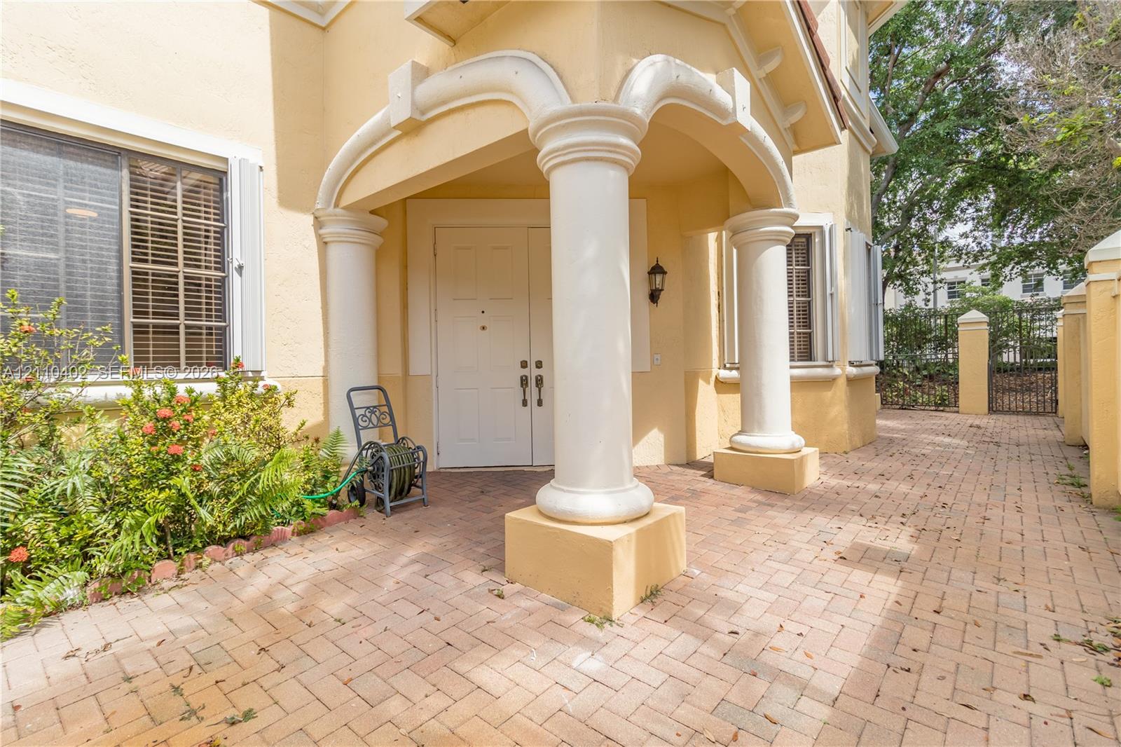 Stucco exterior entry featuring arched portico, structural classical columns, double entry doors, and herringbone-patterned brick paver walkway