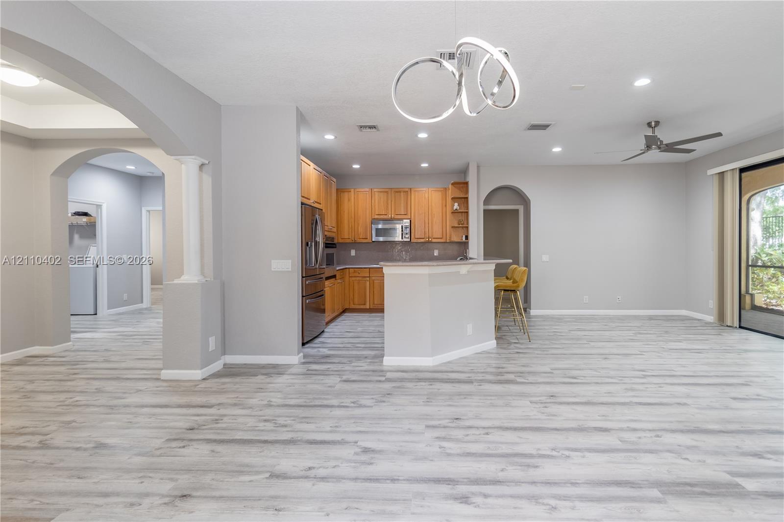 Open-concept interior featuring wood-finish flooring, a modern orbital chandelier, arched architectural columns, natural wood cabinetry, and recessed lighting