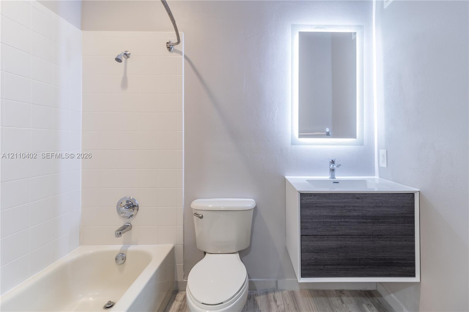 Bathroom featuring a floating vanity with a dark wood-finish cabinet, a rectangular vessel sink, a wall-mounted LED-backlit mirror, and a tile-surround bathtub