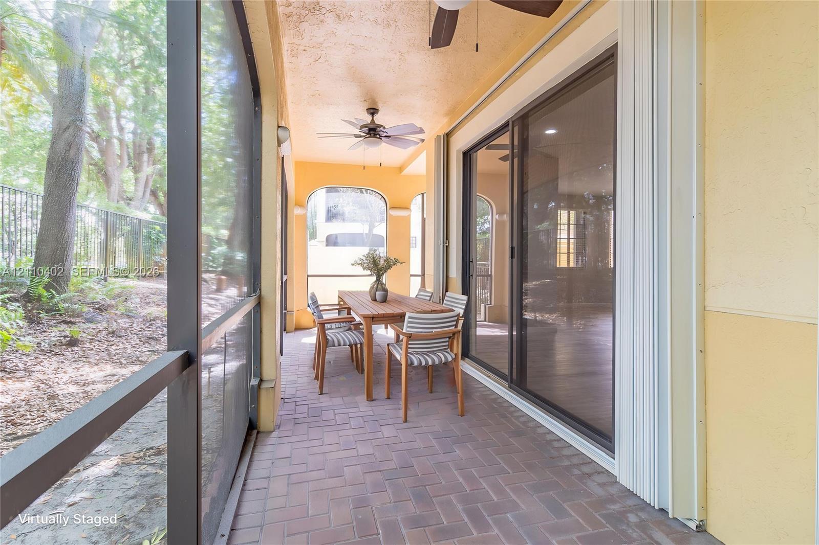 Screened-in covered lanai featuring herringbone-pattern brick paver flooring, dual ceiling fans, and sliding glass door entry