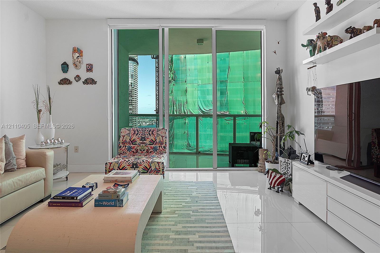 Living area featuring floor-to-ceiling glass sliding doors, built-in white wall shelving, polished tile flooring, and a private balcony