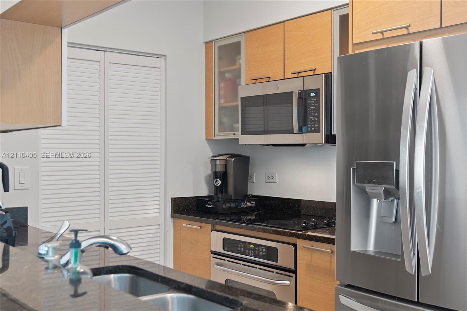 Kitchen featuring light wood-finish cabinetry, dark solid-surface countertops, stainless steel appliances, and a double-basin undermount sink