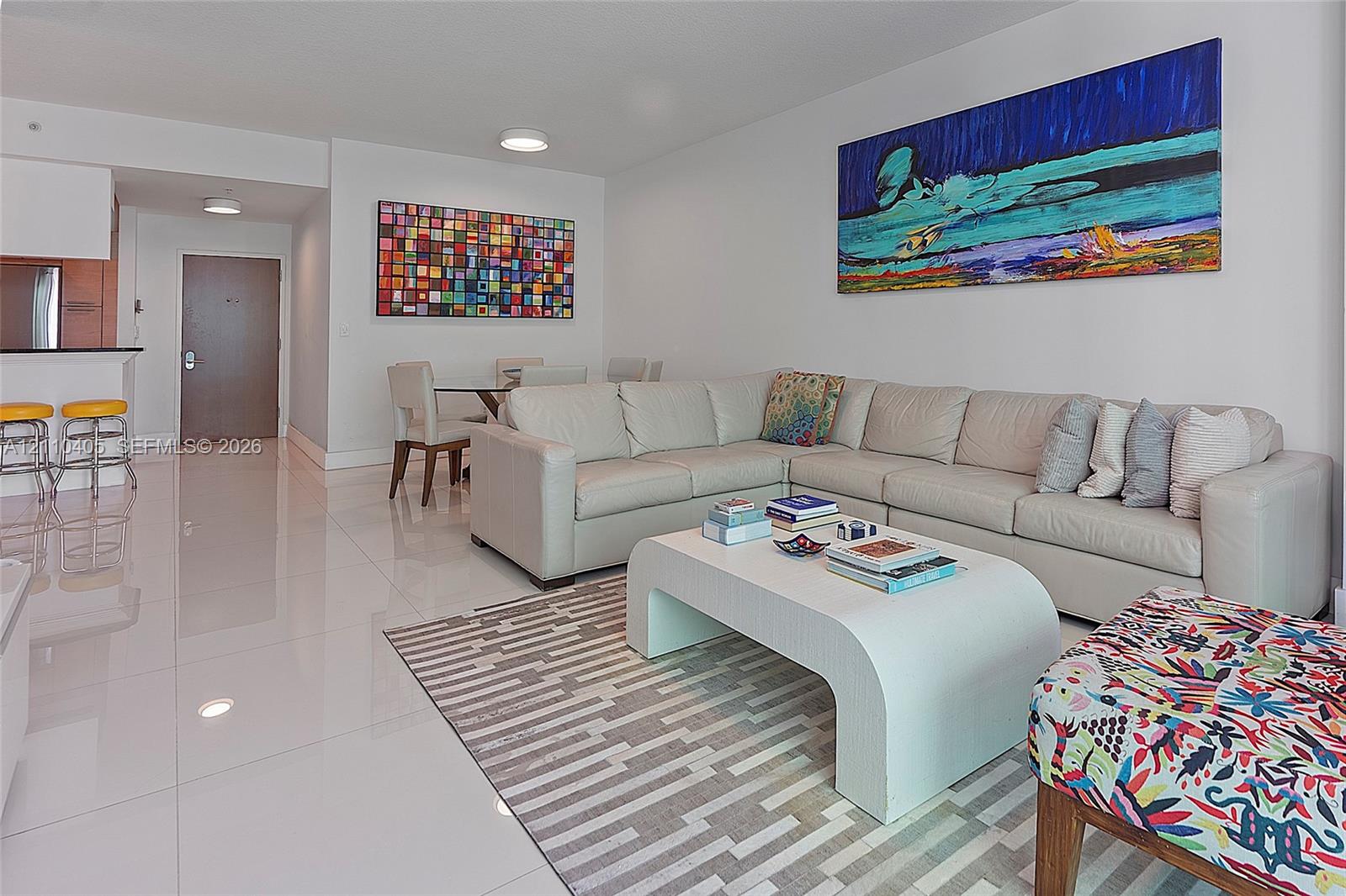 Open-concept interior featuring large-format porcelain tile flooring, recessed ceiling lighting, and a breakfast bar with stone-surface countertop