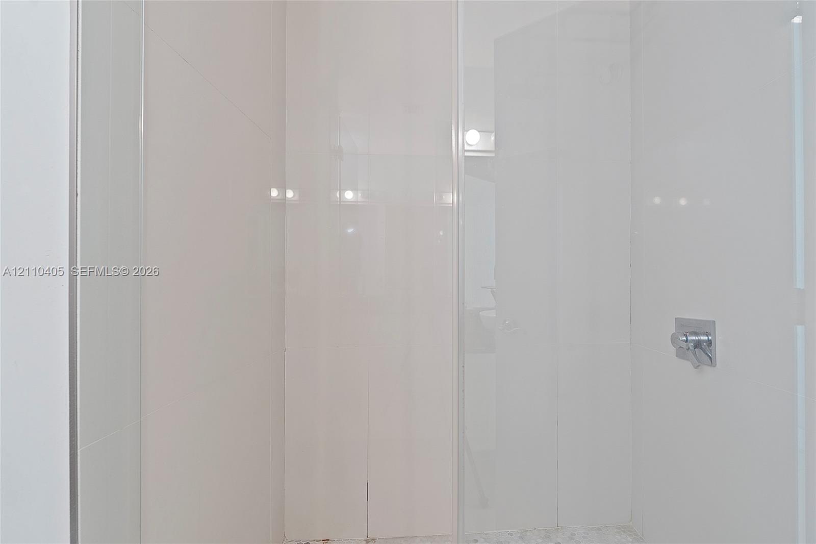 Walk-in shower enclosure with full-height white tile wall surround, glass door, and polished chrome fixtures