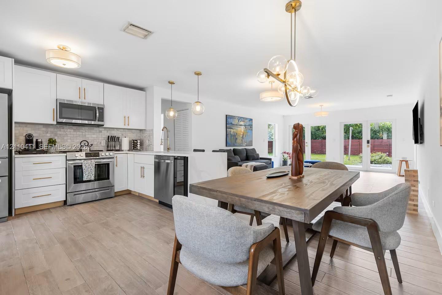 Kitchen featuring white cabinetry, stainless steel appliances, brick-style tile backsplash, wood-finish flooring, and multi-light pendant lighting