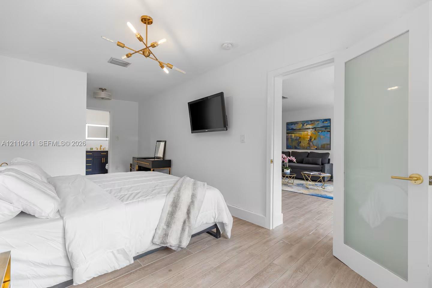 Wood-finish flooring, multi-arm brass finish chandelier, and frosted glass panel door with gold-tone hardware