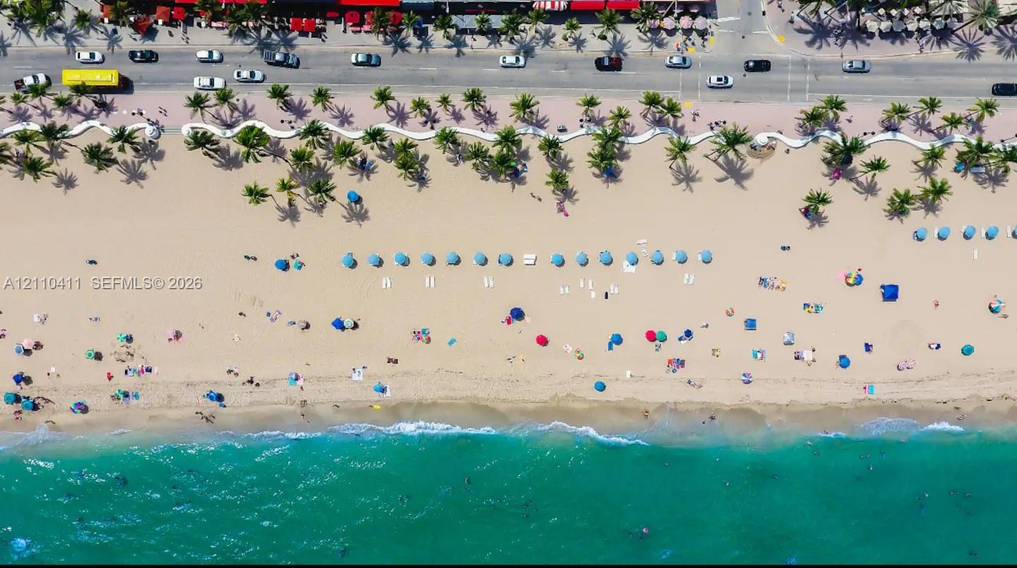 Coastal property featuring direct beach access, expansive sandy shoreline, mature palm tree landscaping, and paved public thoroughfare