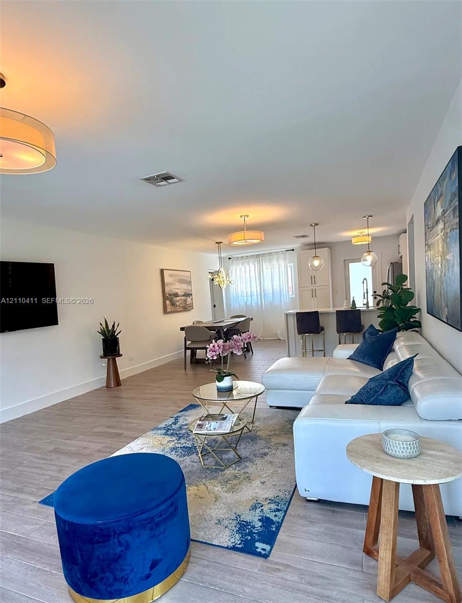 Open-concept interior featuring wood-finish flooring, recessed lighting, neutral wall color palette, kitchen island with breakfast bar, and multiple drum-style pendant light fixtures