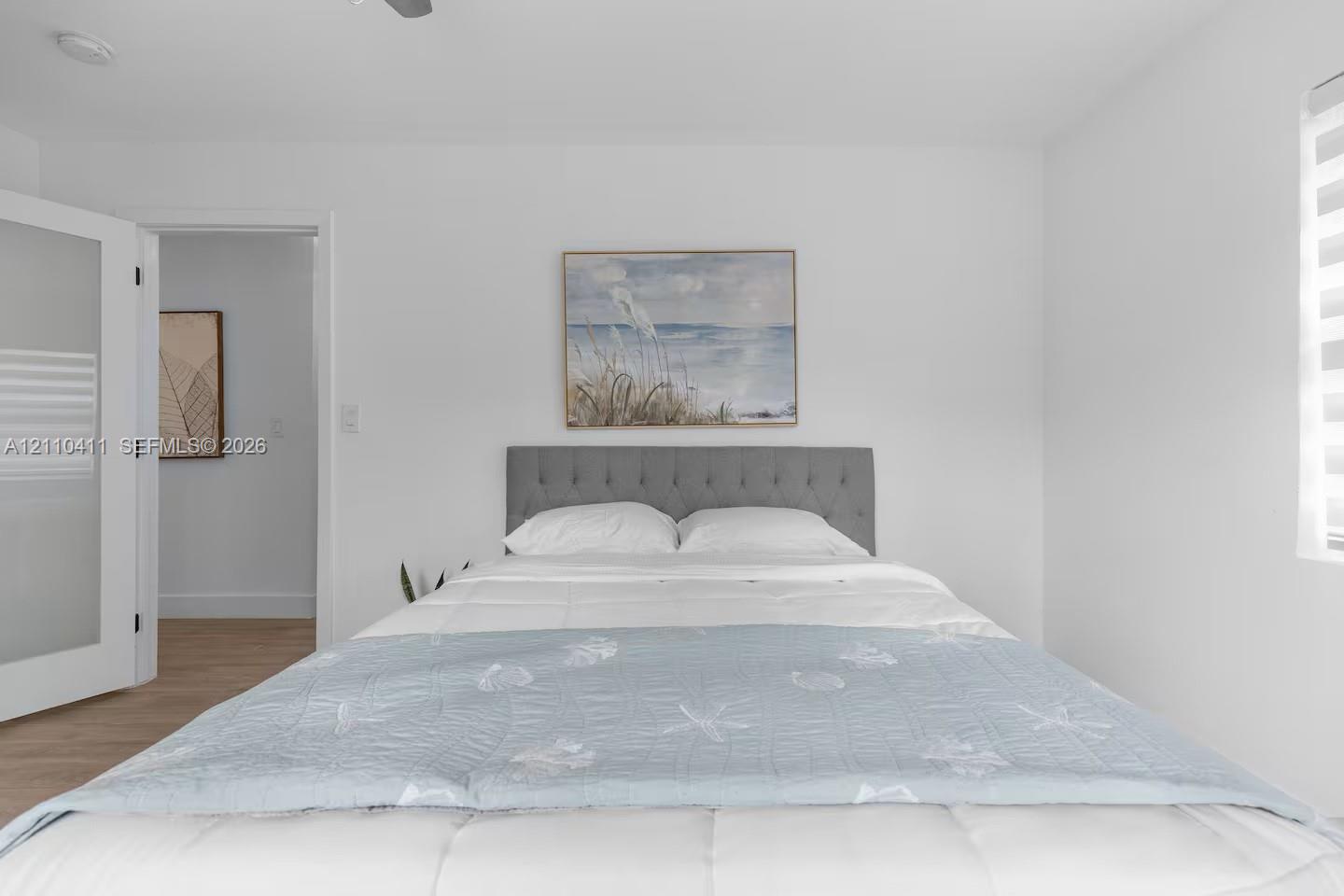 Neutral-toned room featuring wood-finish flooring, a white interior door with frosted glass panels, and a window with horizontal shade treatments