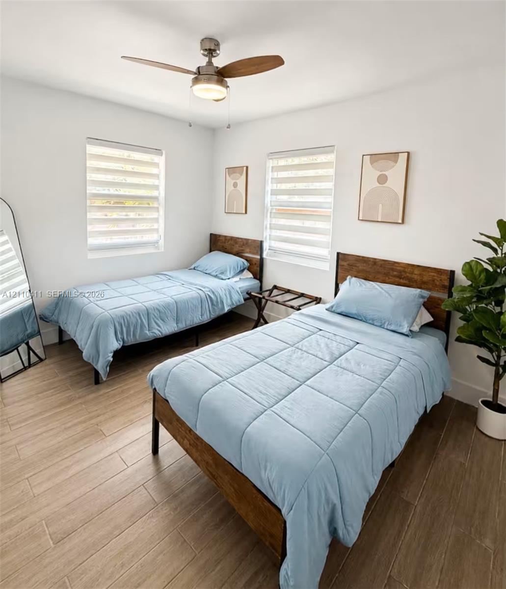 Wood-finish flooring, dual windows featuring horizontal dual-layer shades, and a ceiling-mounted light fixture with integrated fan