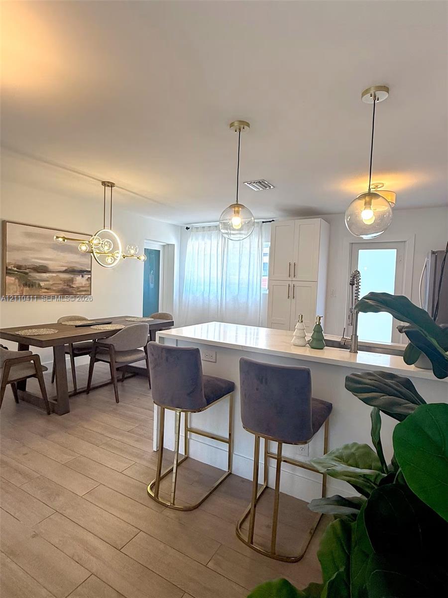 Kitchen featuring a central island with a solid surface countertop, white shaker-style cabinetry, wood-finish flooring, and globe-style pendant lighting