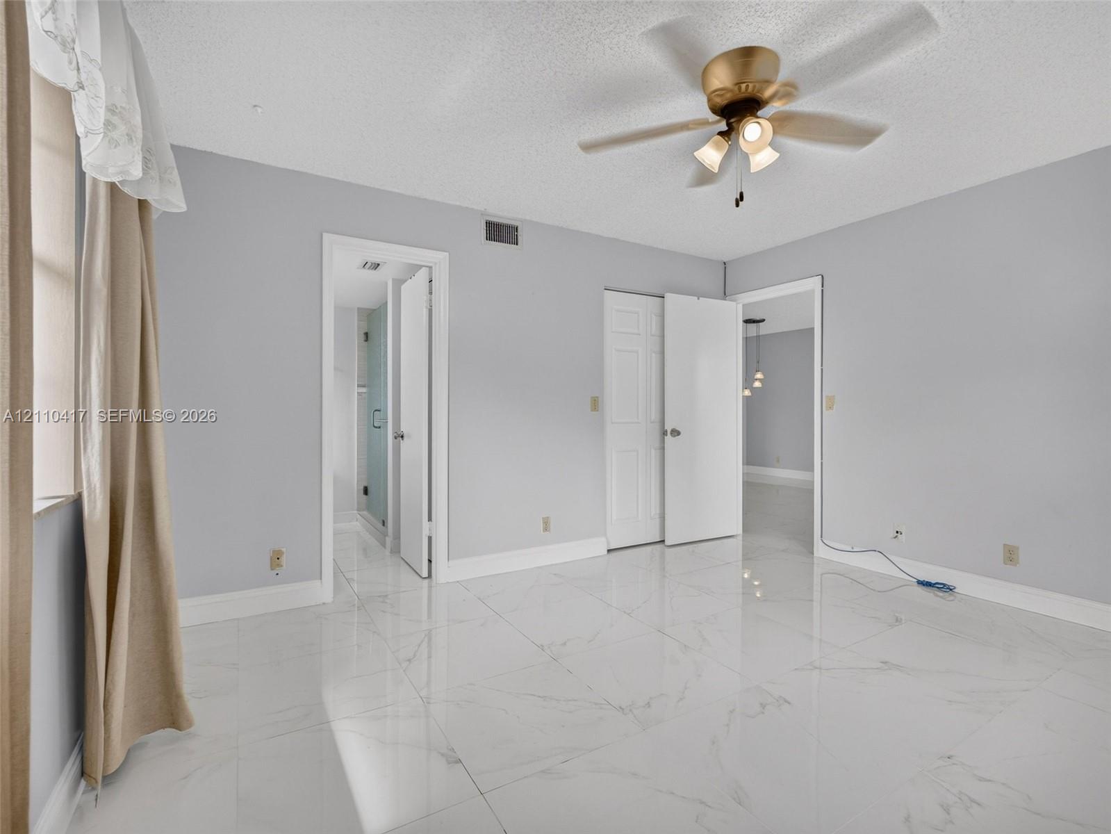 Polished large-format tile flooring with marble-style veining, accented by a brass-finish ceiling fan with integrated lighting and multi-panel doors