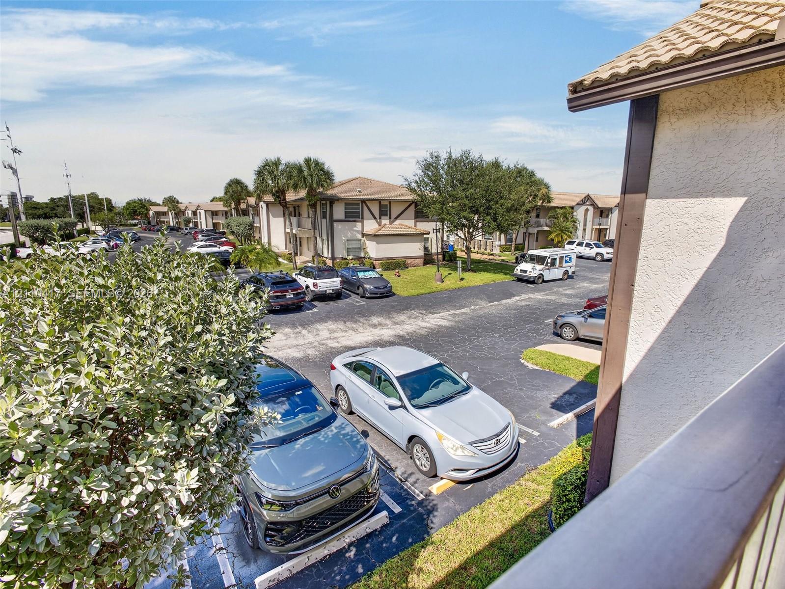 Exterior view featuring multi-story residential buildings with stucco facades and tile roofing, set within a community landscape of established palm trees and paved parking areas