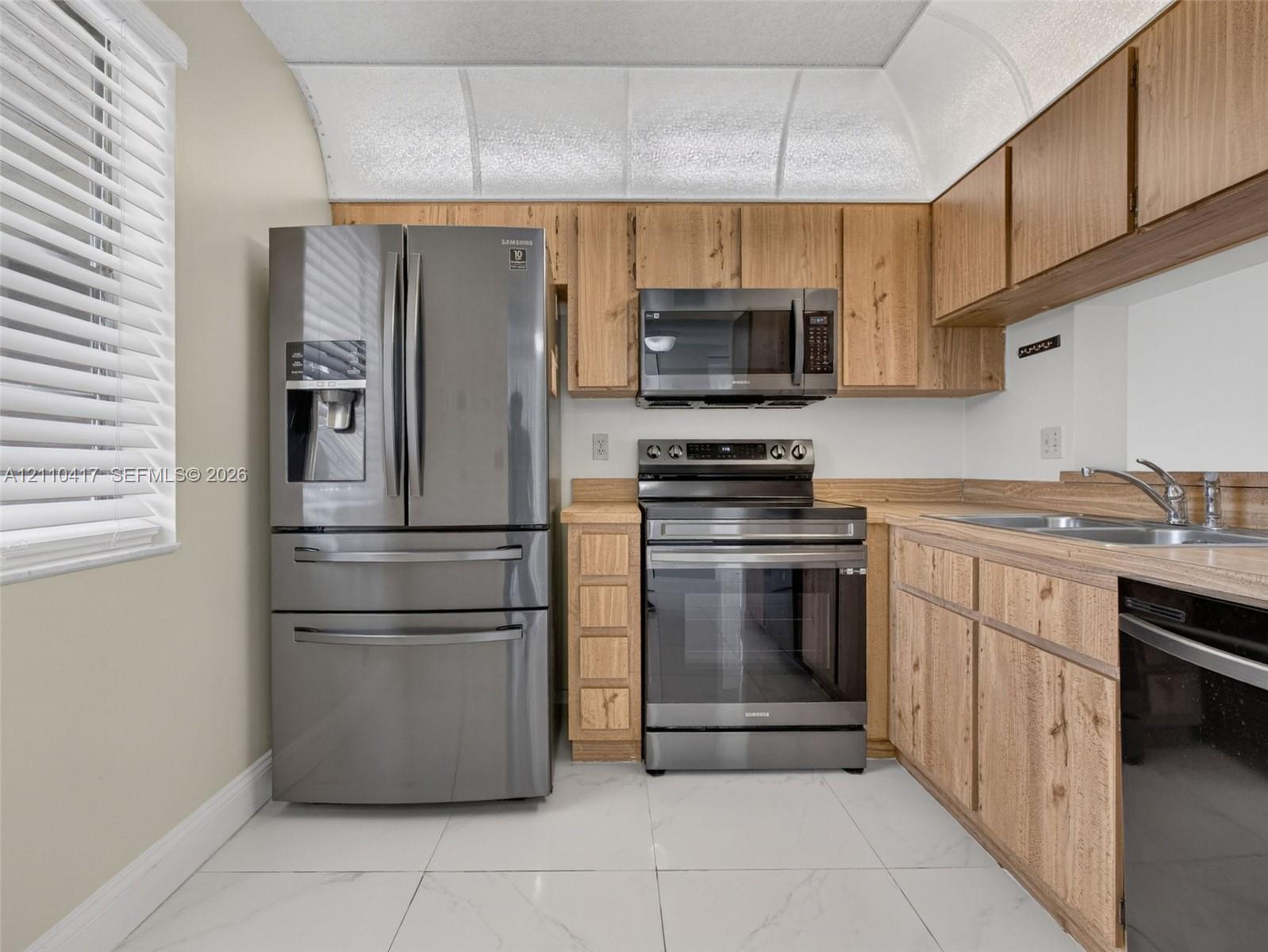 Kitchen featuring wood-finish cabinetry, stainless steel appliances, a double-basin stainless steel sink, and light-toned tile flooring