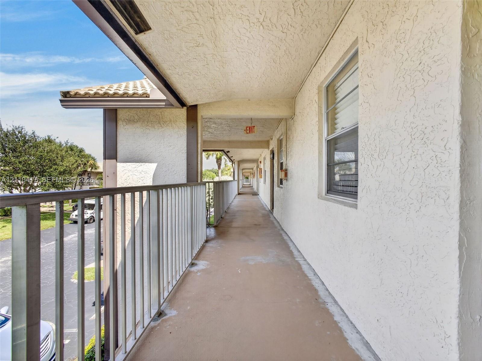 Covered exterior walkway featuring stucco walls, metal railings, and concrete flooring
