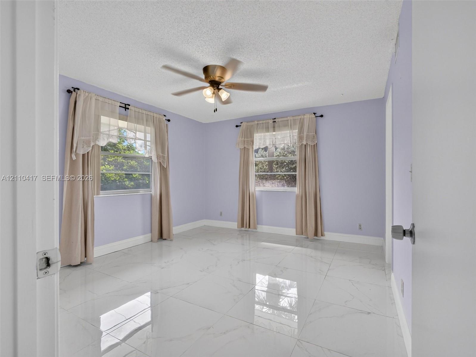Large-format polished tile flooring, ceiling fan with integrated lighting, and multiple windows providing natural light
