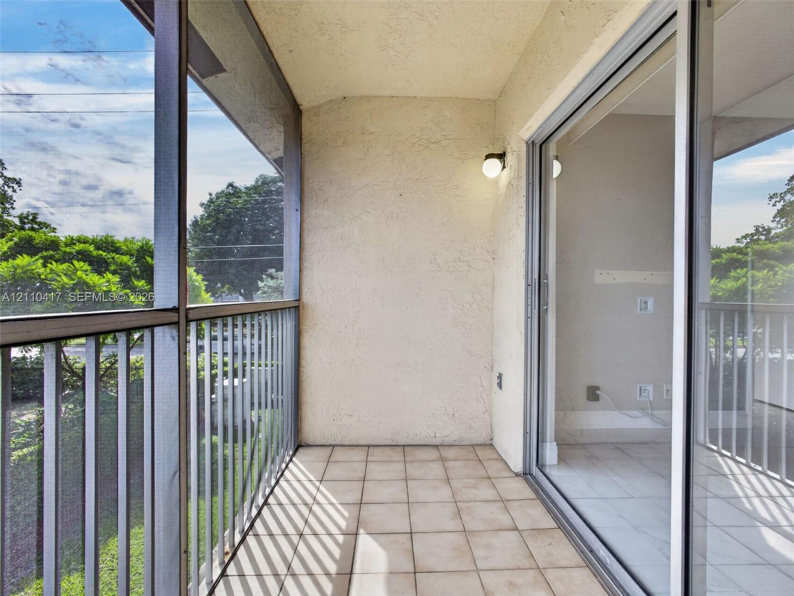 Screened-in balcony featuring light-toned ceramic tile flooring, a textured stucco wall finish, metal railing, and a sliding glass door