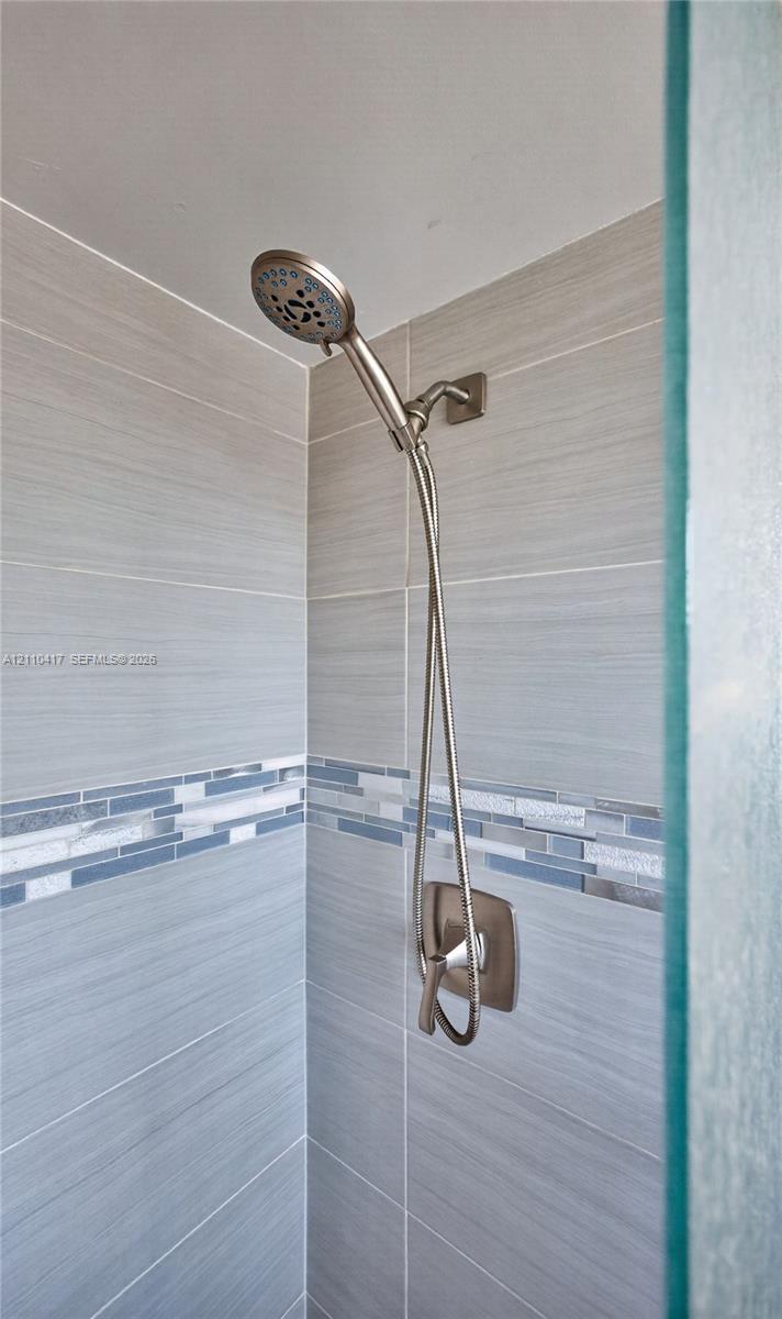 Shower enclosure featuring brushed nickel handheld showerhead, single-handle pressure balance valve, horizontal neutral-toned wall tile, and decorative glass mosaic accent border