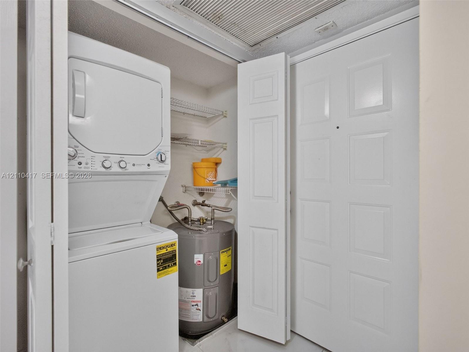 Utility closet featuring a stacked washer and dryer, integrated electric water heater, and wire shelving
