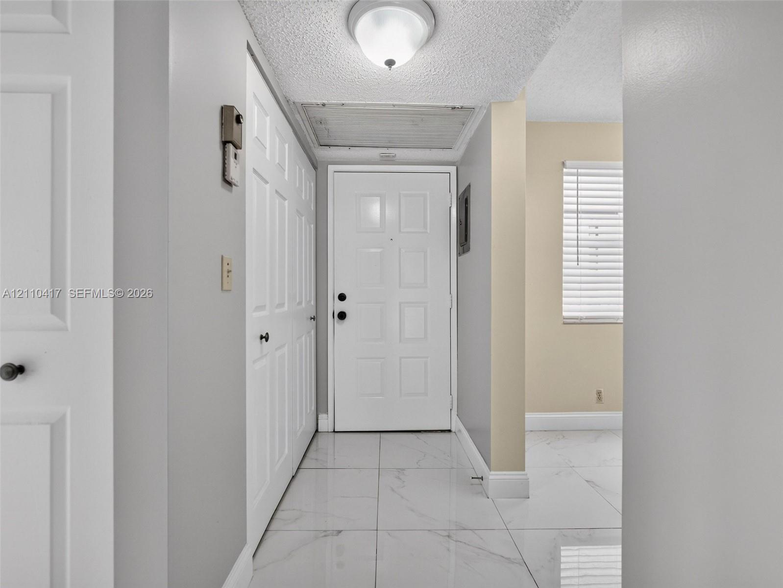 Entryway featuring large-format white tile flooring, paneled white interior doors, a flush-mount ceiling fixture, and a white paneled exterior door
