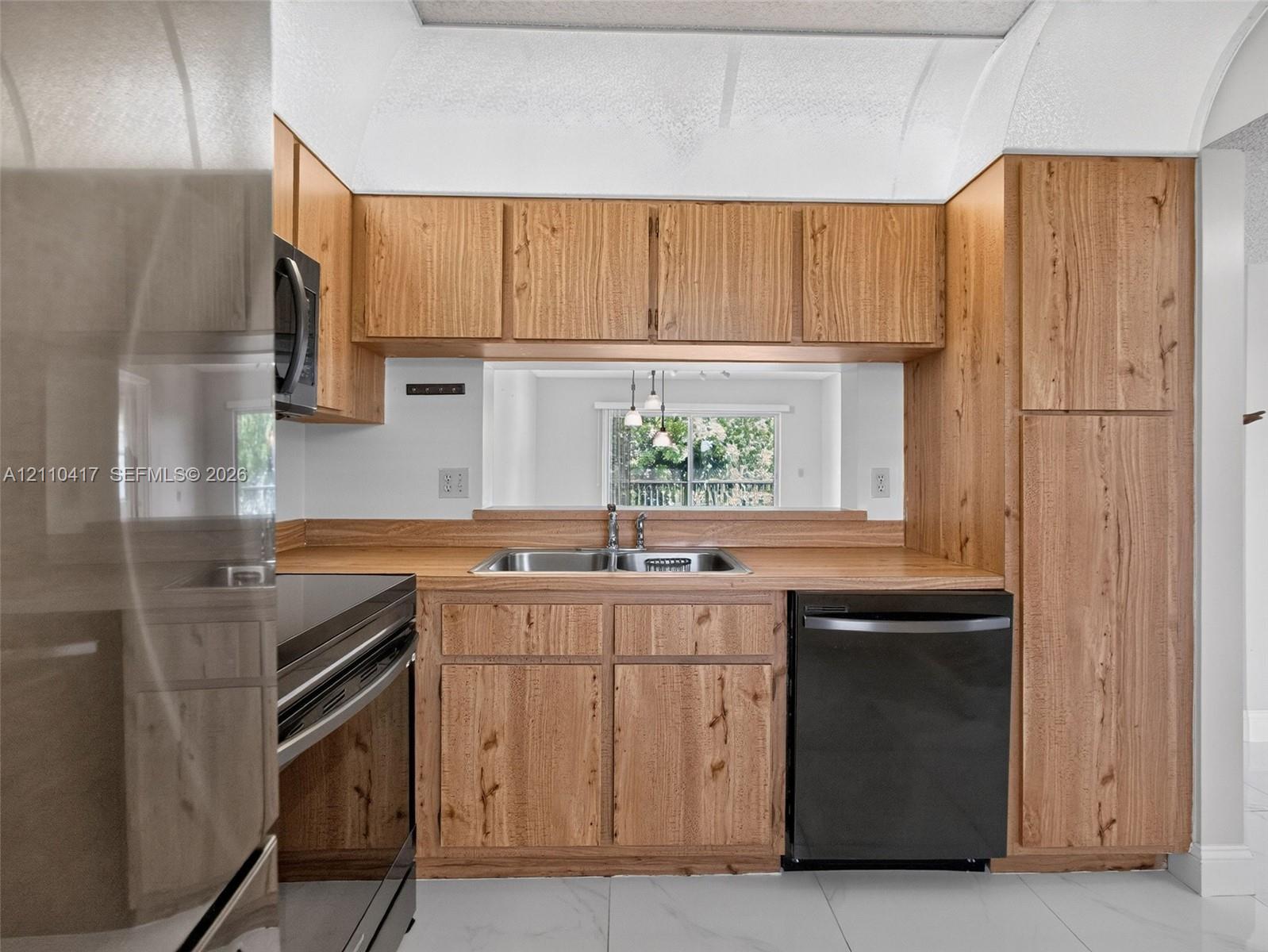 Kitchen featuring natural wood-finish cabinetry, a dual-basin stainless steel sink, black appliances, and white stone-patterned flooring