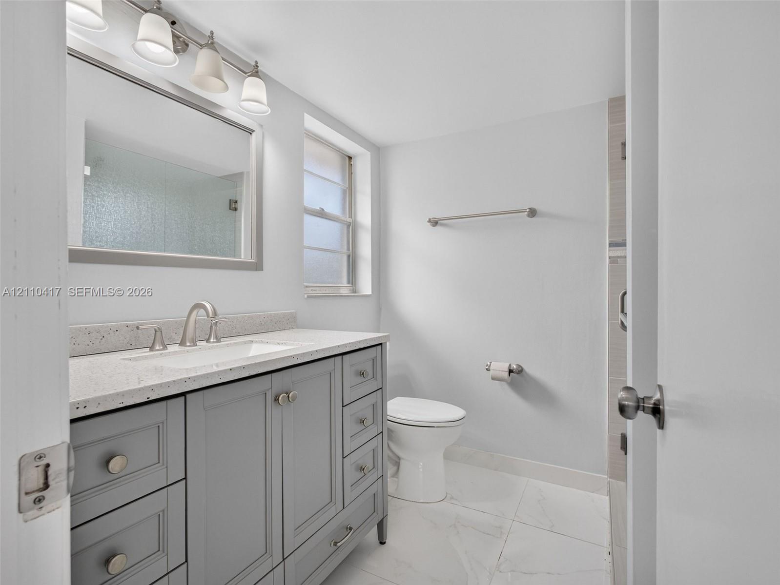 Bathroom featuring a grey shaker-style vanity, stone-composite countertop with an integrated basin, multi-drawer storage, polished nickel-finish hardware, and large-format porcelain floor tile