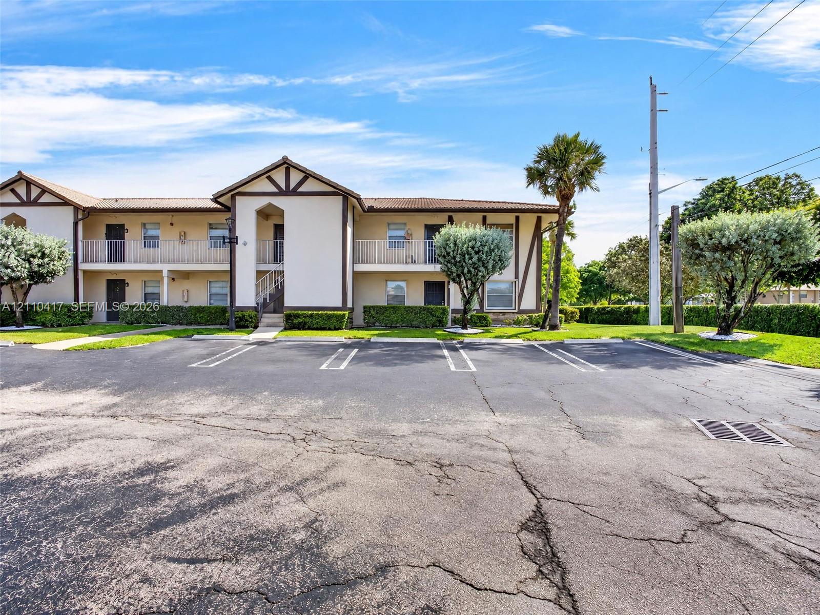 Two-story stucco exterior featuring timber-framed accents, upper-level railed balconies, covered ground-level entrances, and mature landscaping