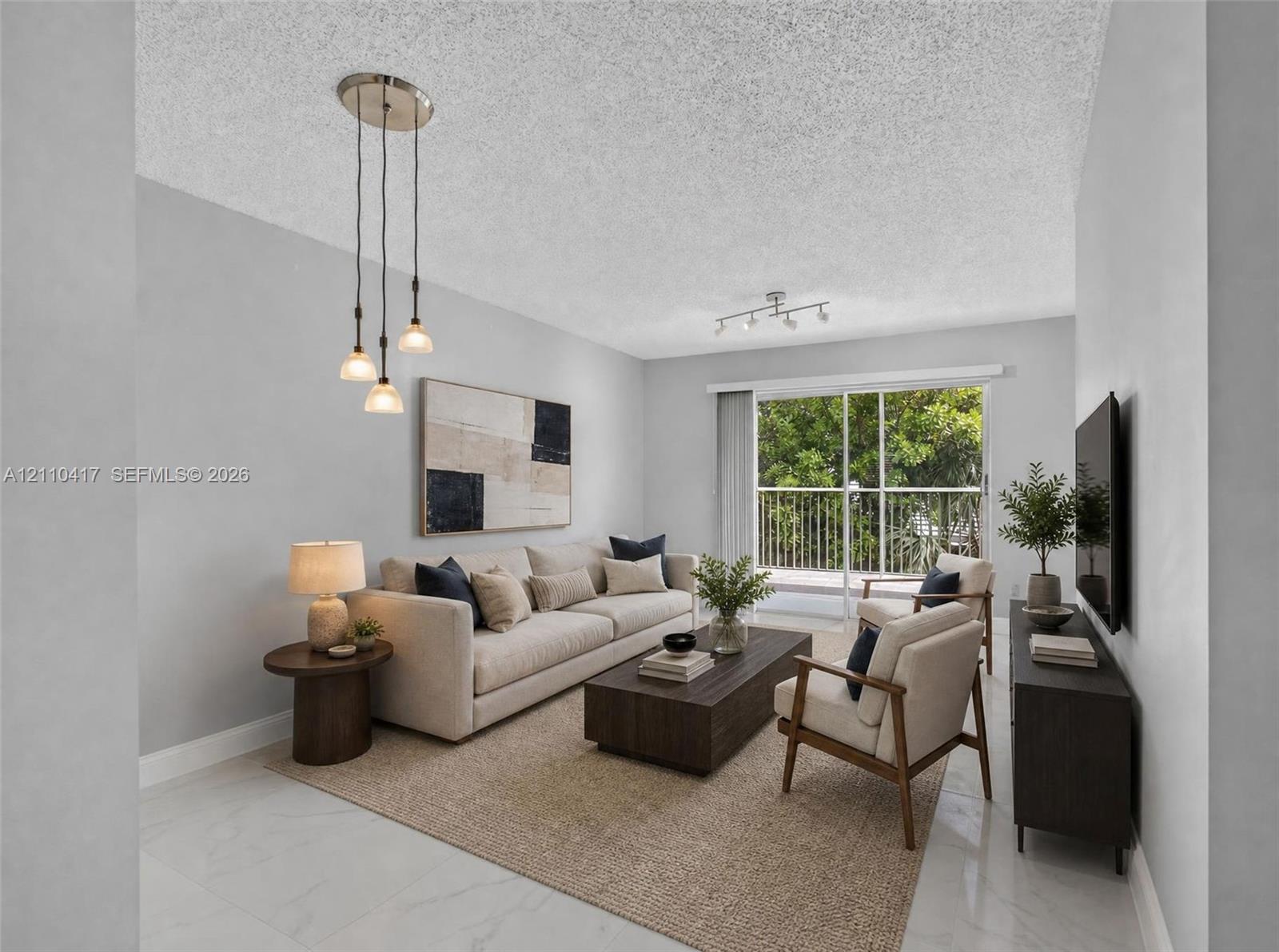 Living area featuring neutral-toned walls, tile flooring, a multi-light pendant fixture, a secondary track lighting fixture, and glass sliding doors providing external access to a railed balcony