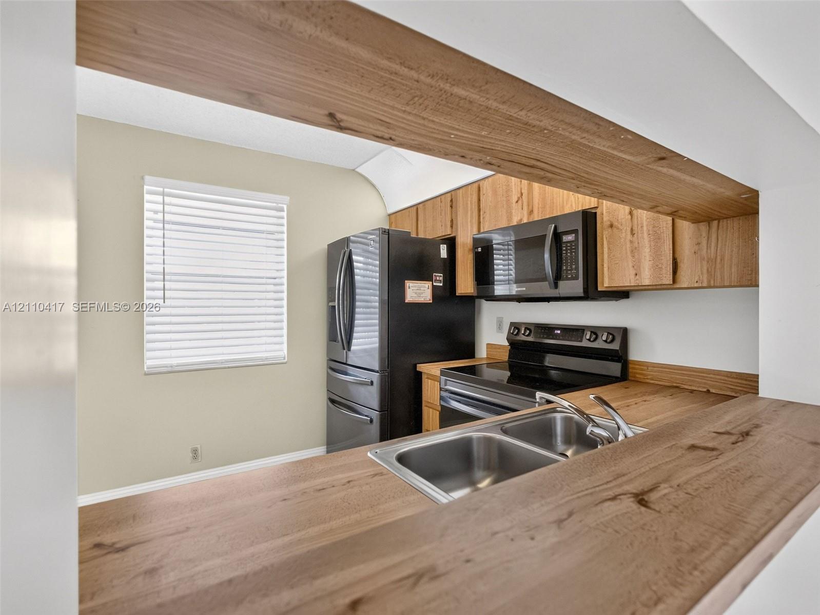Kitchen featuring wood-finish countertops, natural wood cabinetry, stainless steel dual-basin sink, and black appliances including a built-in microwave