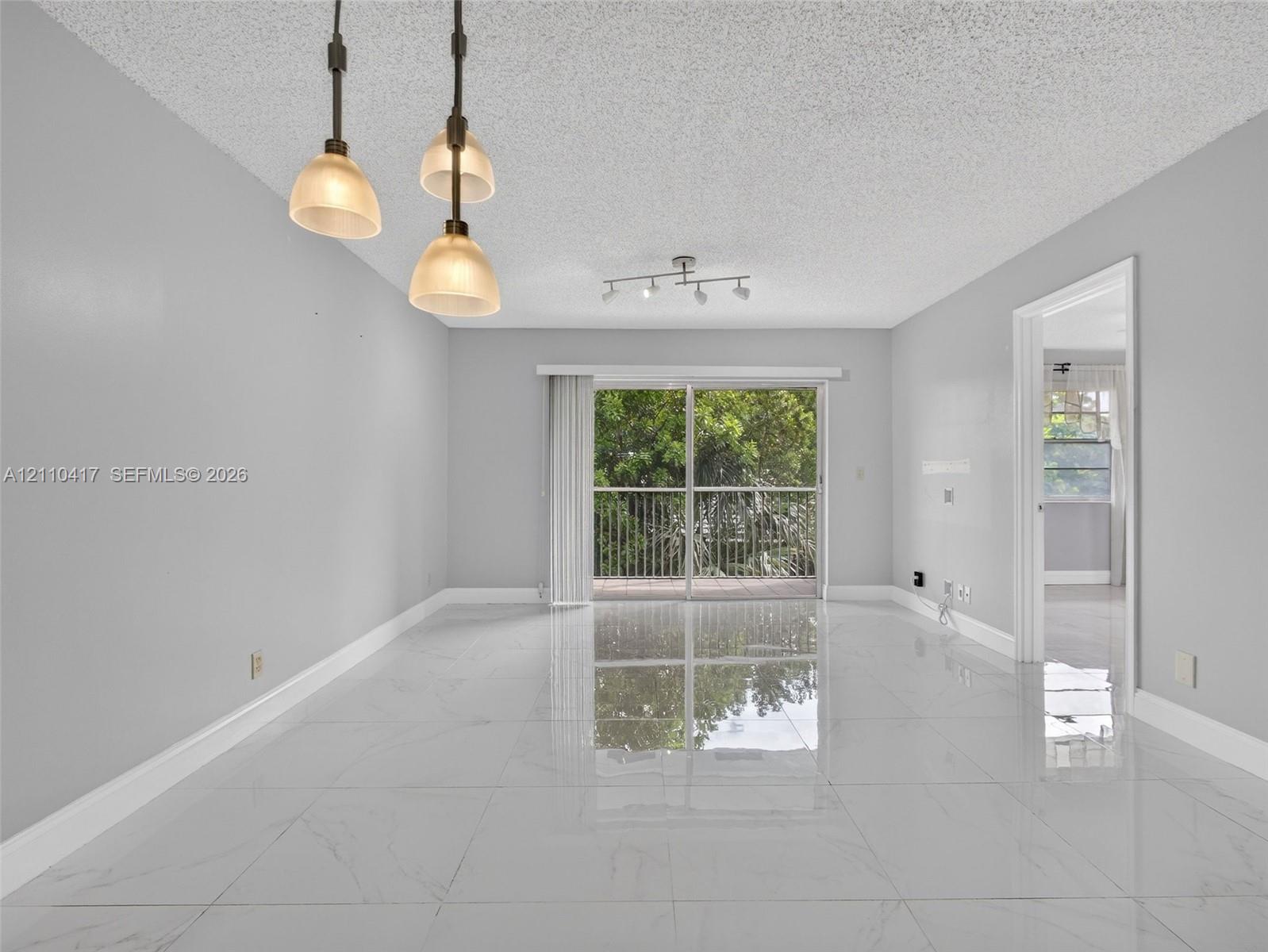Large-format polished porcelain tile flooring, sliding glass door with balcony access, triple-pendant light fixture, and multi-directional track lighting