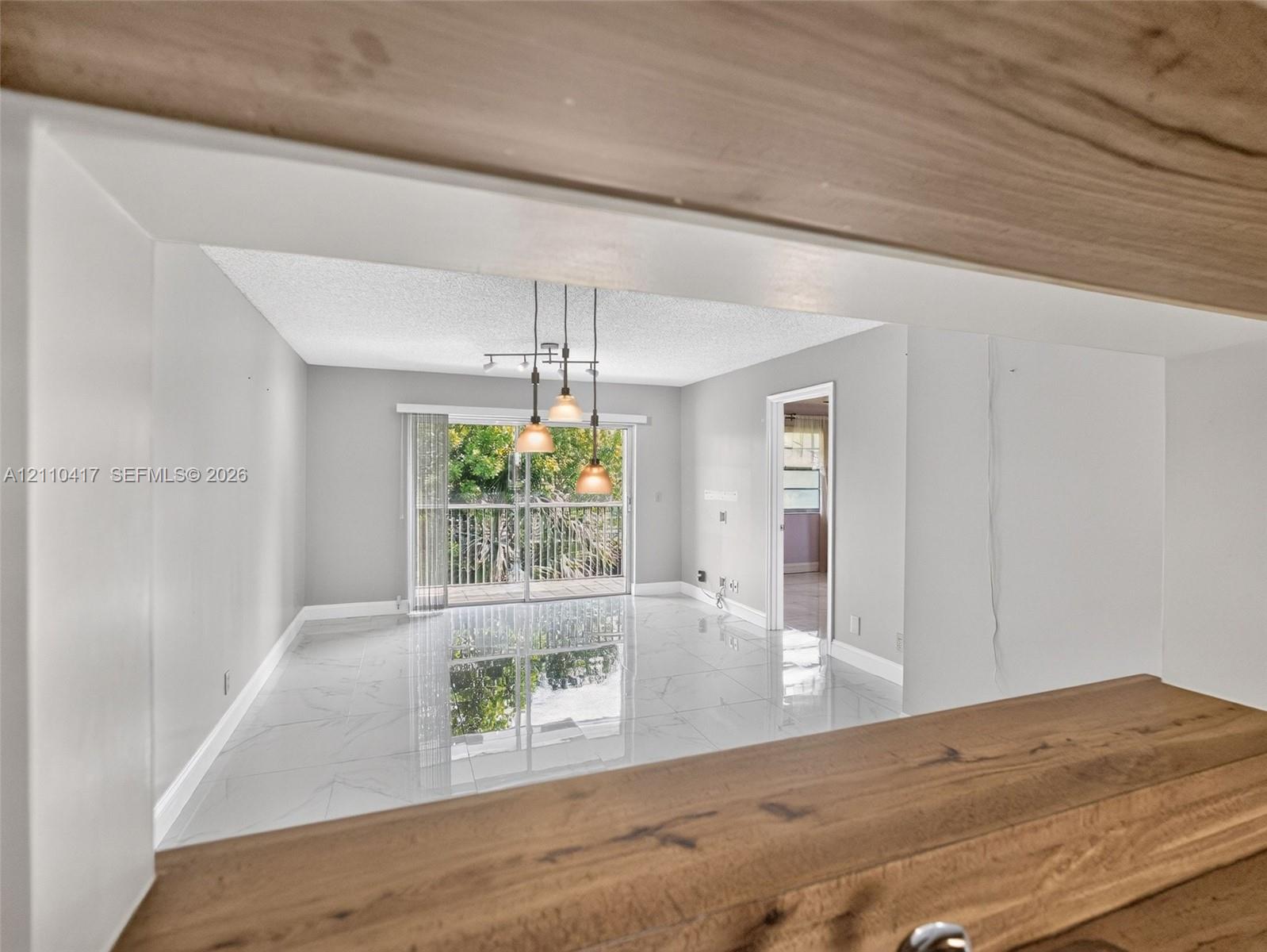 Polished tile flooring, wood-finish breakfast bar, three-pendant drop lighting, and sliding glass door with balcony access
