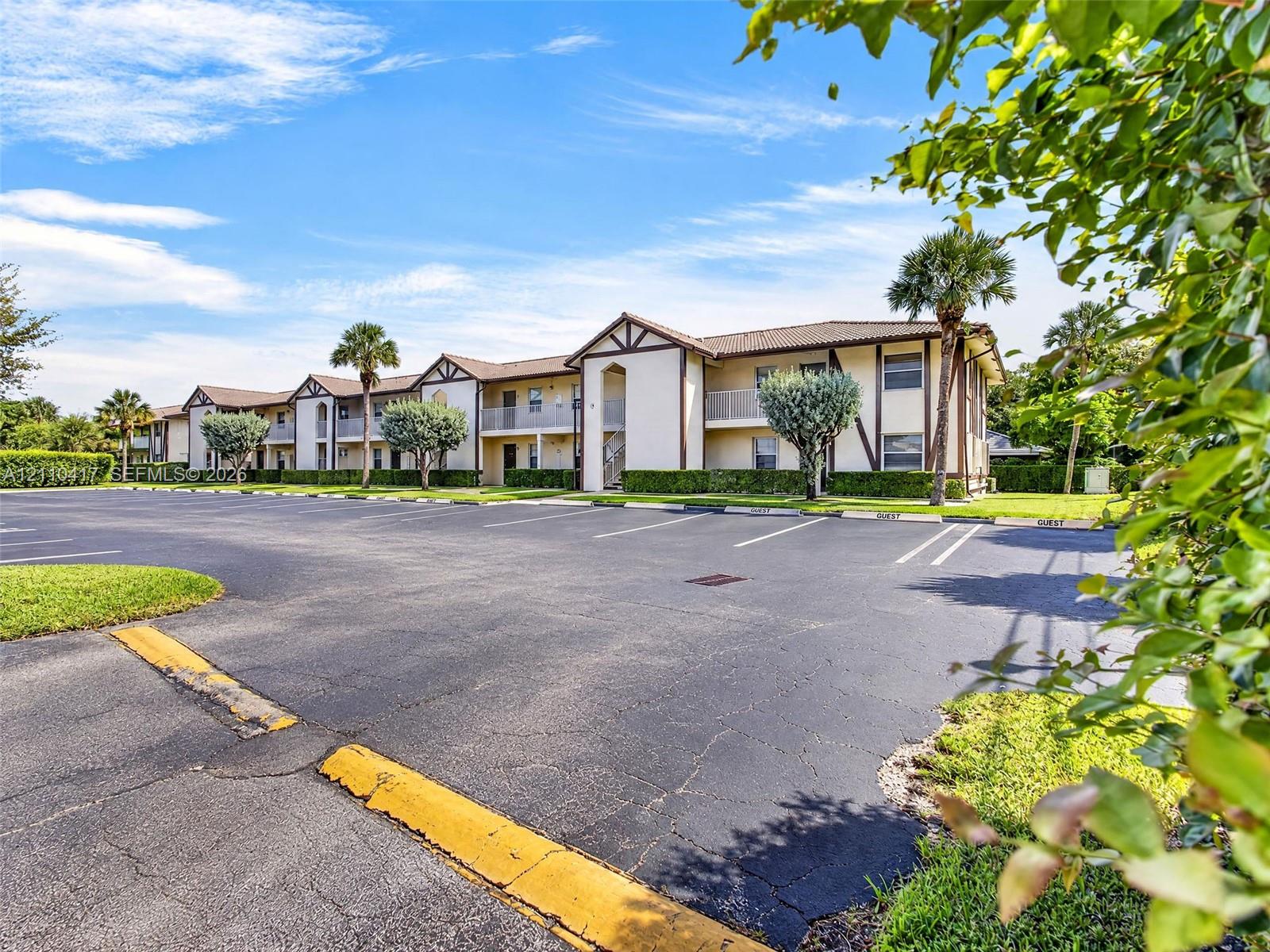 Two-story building featuring a neutral stucco exterior, brown trim, multi-gabled roofline, private balconies, and dedicated asphalt parking