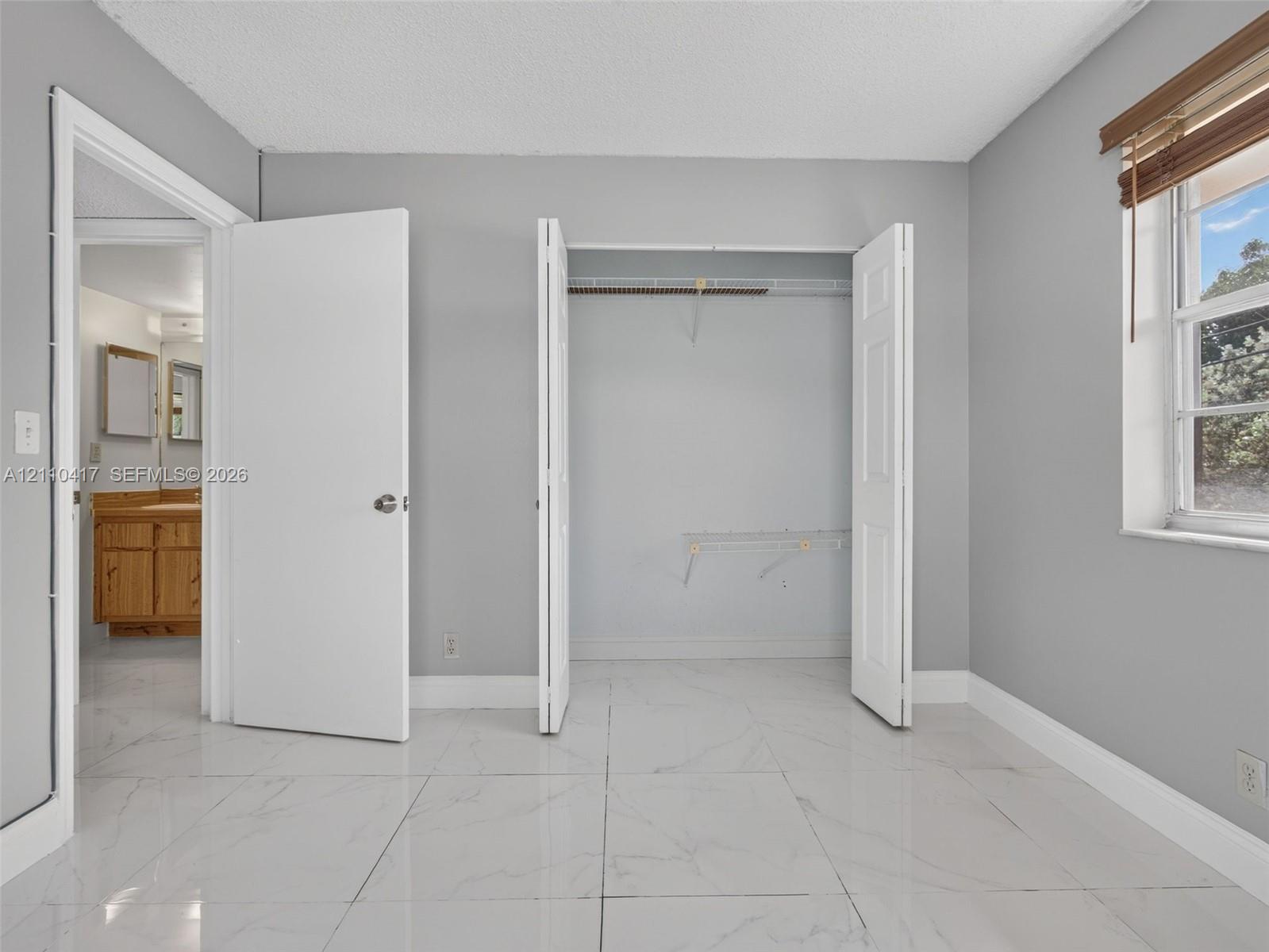 Neutral-toned interior featuring large-format tile flooring, a dual-door closet with built-in wire shelving, and a window with wood-finish blinds