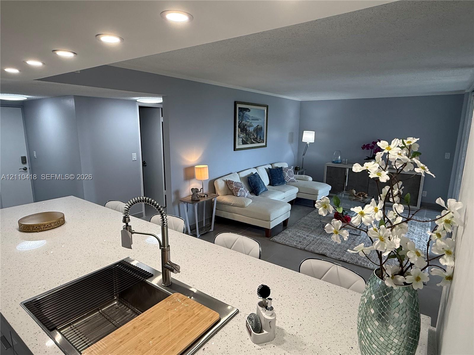 Kitchen featuring a quartz countertop island, undermount stainless steel sink, and high-arc pull-down faucet, recessed ceiling lighting, and solid-finish walls