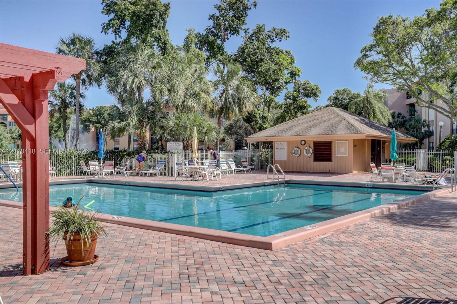 Swimming pool with a brick-paver deck, pergola structure, and poolside cabana surrounded by mature palm trees