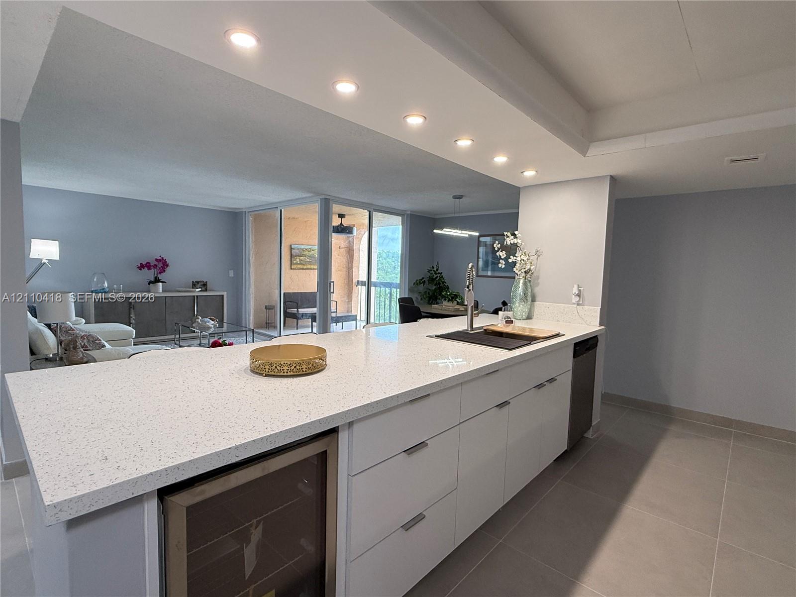 Kitchen island featuring a stone-composite countertop, white flat-panel cabinetry, a built-in wine refrigerator, and recessed lighting