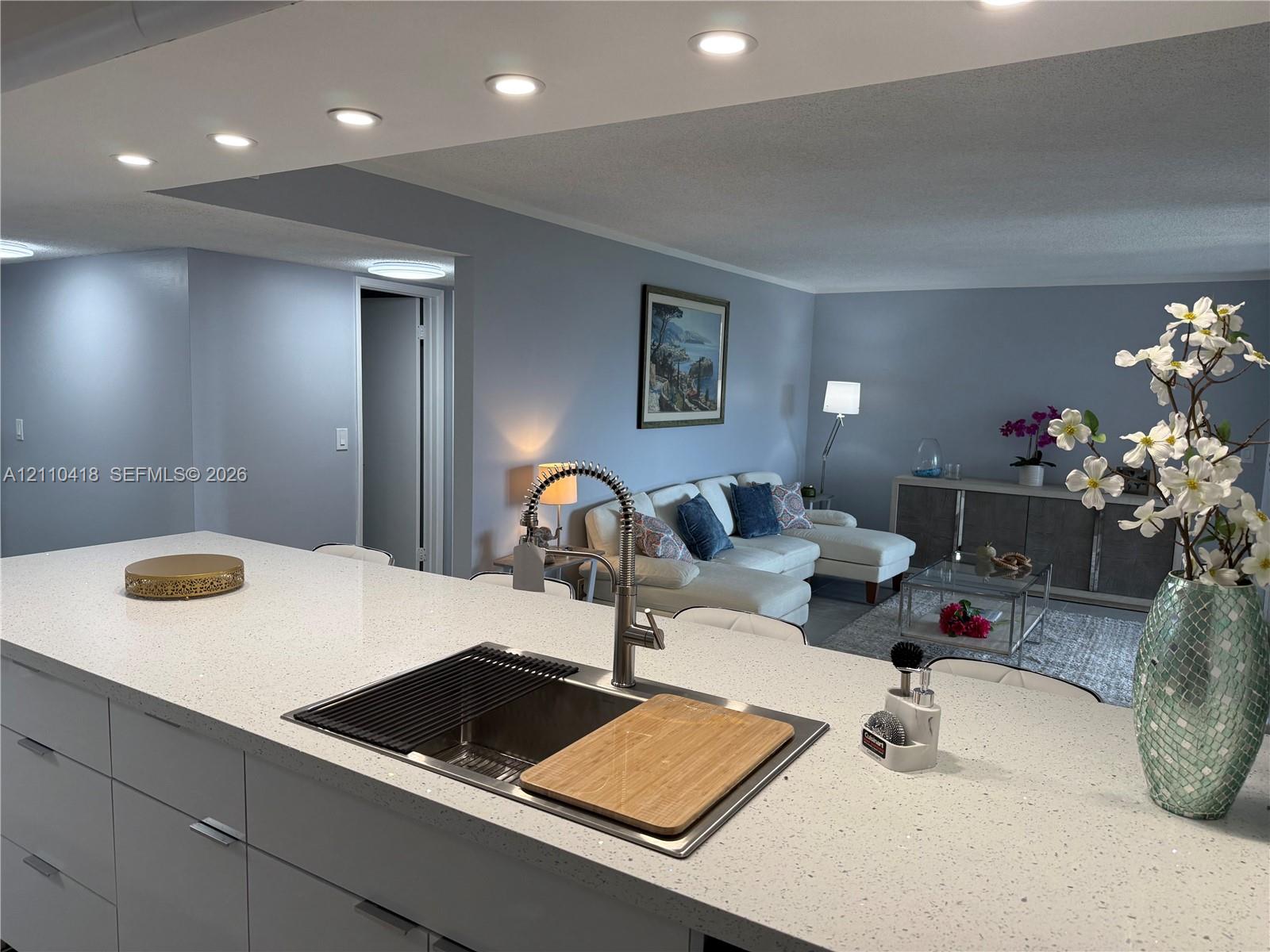 Kitchen island featuring a stone-composite countertop, undermount stainless steel sink, gooseneck faucet, and flat-panel cabinetry with recessed lighting